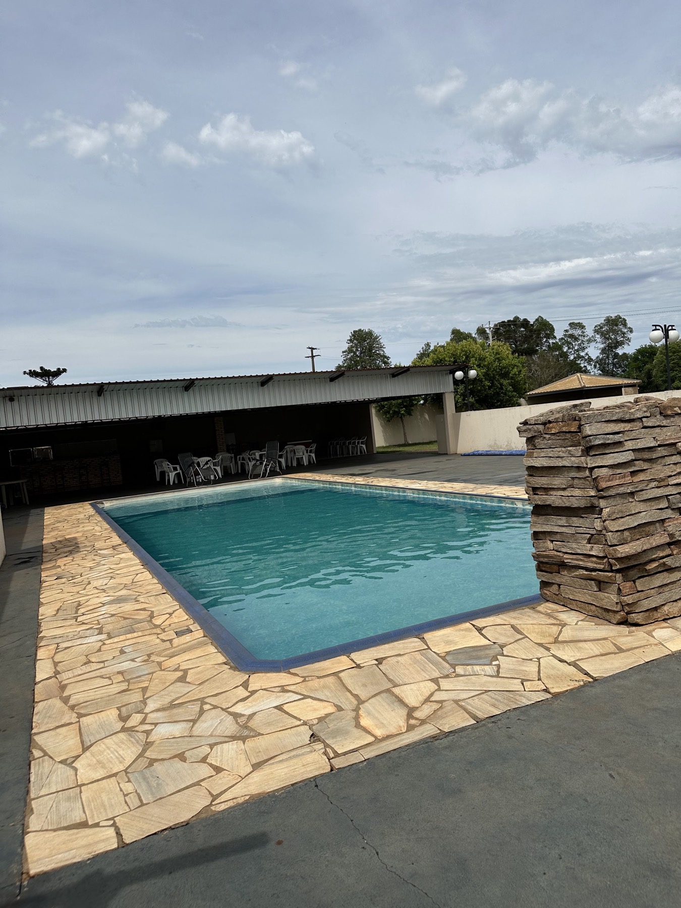 Piscina com borda de pedra e área coberta ao fundo